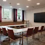 A modern conference room at Home Hotel Uppsala with a U-shaped table, chairs, large windows, and a wall-mounted screen.