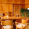 Wooden mid-century modern desk and chair set in a warm, paneled room with decorative items and plants, reflective of retro interior design.