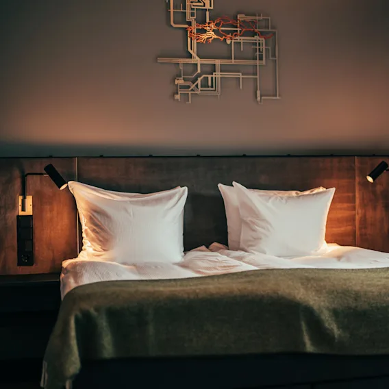 Viihtyisä hotellihuone, jossa on suuri sänky, valkoiset tyynyt ja lämmin valaistus, täydellinen rentoutumiseen.
