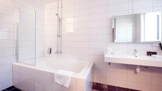 Ett rent, kaklat badrum med badkar, dusch, spegelskåp och handfat.