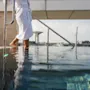 Henkilö valkoisessa kylpytakissa astumassa uima-altaaseen Quality Hotel Öresundissa, kaupunkinäkymä taustalla.