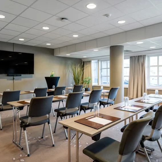 A modern conference room with rows of tables and chairs facing a large screen, ready for a meeting or presentation.