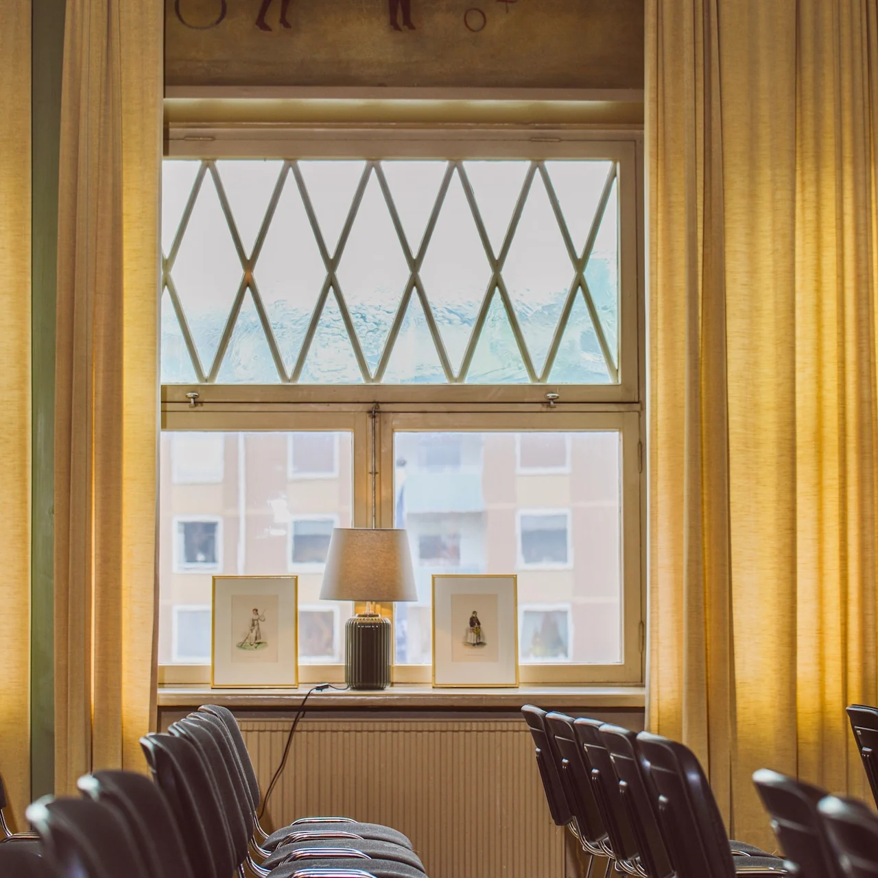 Rows of empty chairs face a window with a framed painting and lamp on a shelf. A mural of an ox is above, labeled "Oxen."
