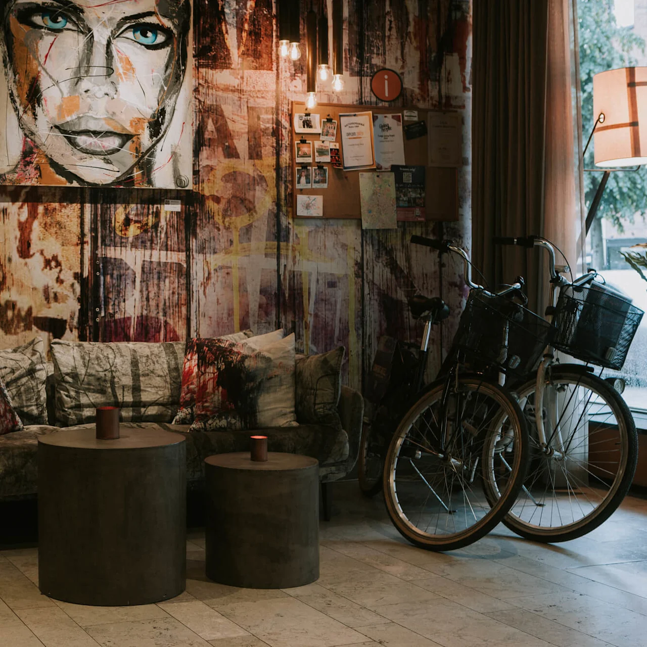 En hyggelig lounge med kunstprydede vægge, sofa, betonborde og en cykel.