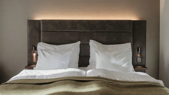 Kutsuva hotellisänky raikkailla valkoisilla tyynyillä ja lämpimällä ruskealla peitolla, valmiina rentouttavaan oleskeluun Home Hotel Victoriassa.