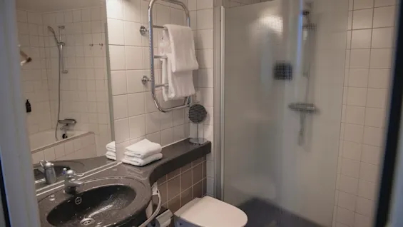 A clean and modern bathroom at Home Hotel Uppsala, featuring a sink, toilet, shower, white tiles, and fresh towels.
