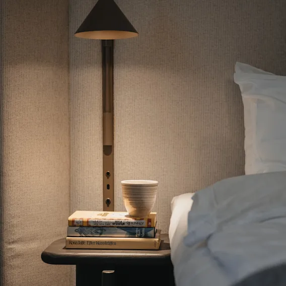 En mysig sängscen på Home Hotel Victoria med en hög böcker, en kopp och en varm lampa, som inbjuder till avkoppling.