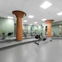 Et romslig hotellgym med treningsapparater, grønne vegger og store oransje søyler.