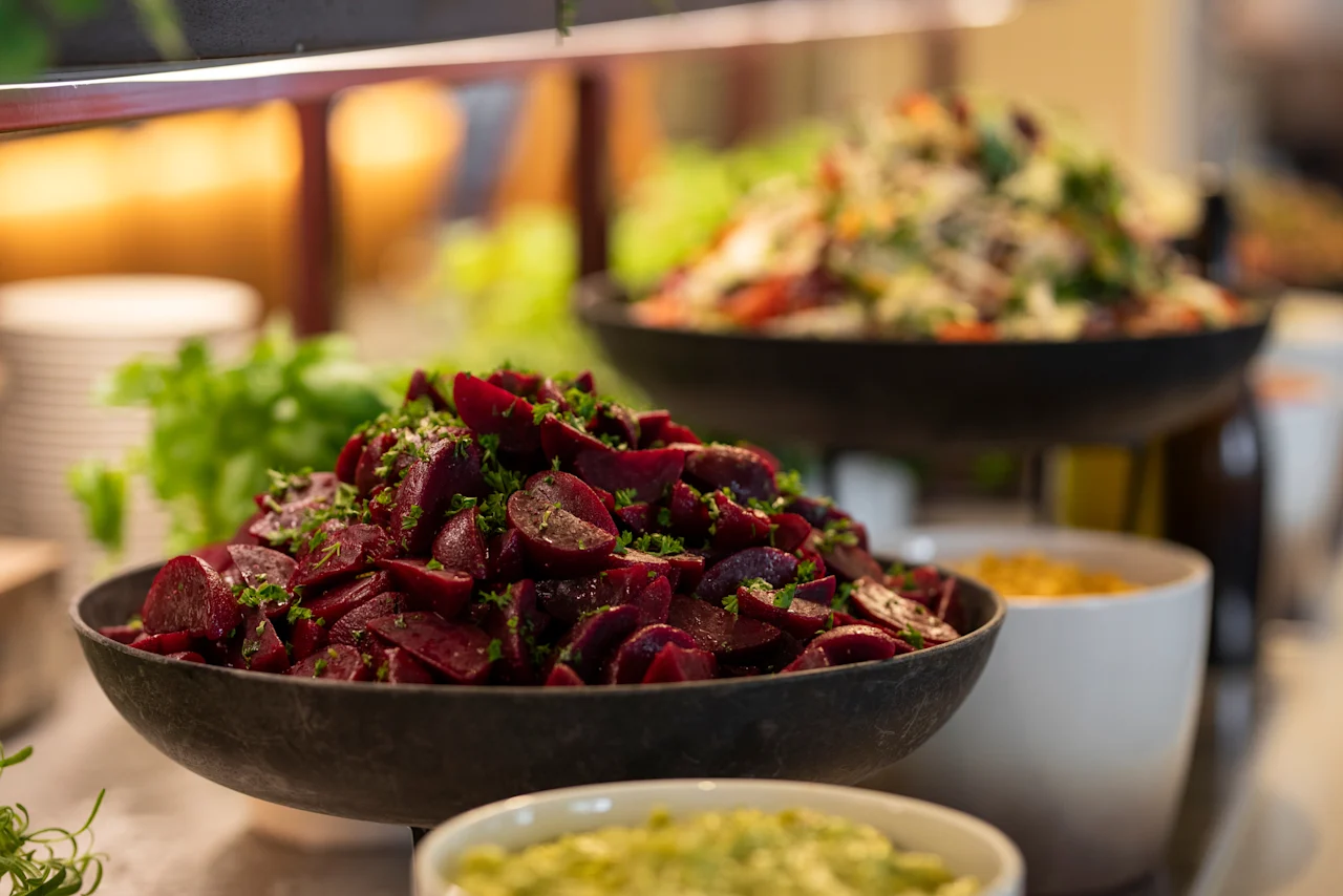 Ett färgstarkt bufféutbud, med en framträdande skål med skivade rödbetor och färska gröna örter, tillsammans med andra hälsosamma salladsalternativ.
