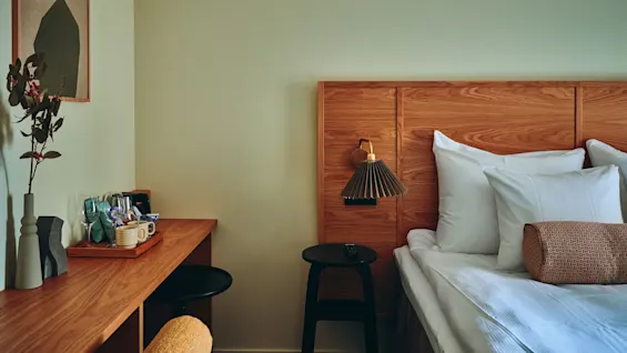 Et koselig hotellrom med en komfortabel seng, en sengegavl i tre, et skrivebordsområde og en varm, innbydende atmosfære.