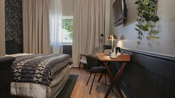 Ett inbjudande hotellrum med en säng, en funktionell skrivbordsplats och naturligt ljus från ett fönster, vilket skapar en avkopplande atmosfär.