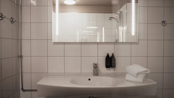 A clean, modern bathroom with white tiled walls, a sink, a lighted mirror, and fresh towels, ready for use.