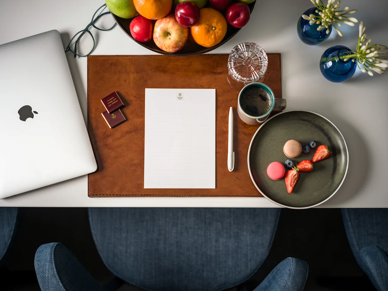 Ett prydligt arrangerat skrivbord med en laptop, färsk frukt, kaffe och en söt godsak, vilket antyder en produktiv och trevlig arbetsplats.