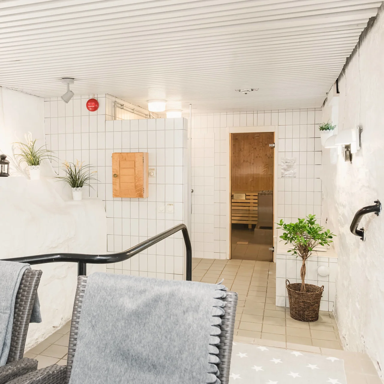 A cozy spa area with lounge chairs, towels, plants, and lanterns, leading to a wooden sauna door.