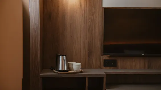 Et innbydende hotellromhjørne med vannkoker og kopper for en varm drikke, og en TV, integrert i stilfull trepanel.