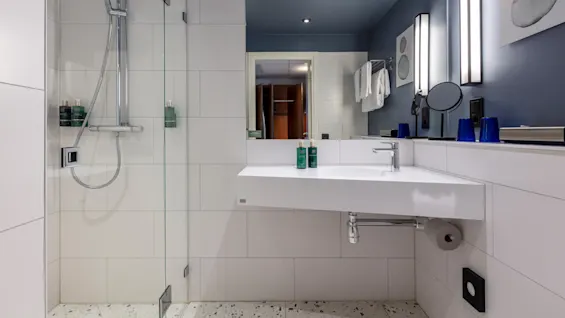 Modern bathroom interior with a floating vanity, mirror, shower area, and blue accents within a home setting.