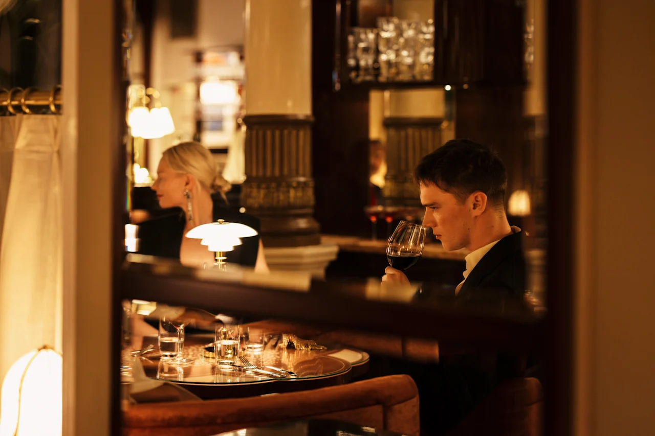 Henkilö nauttimassa lasillisen punaviiniä hienostuneessa baariympäristössä. Hotel Kämp – Kämp Bar.