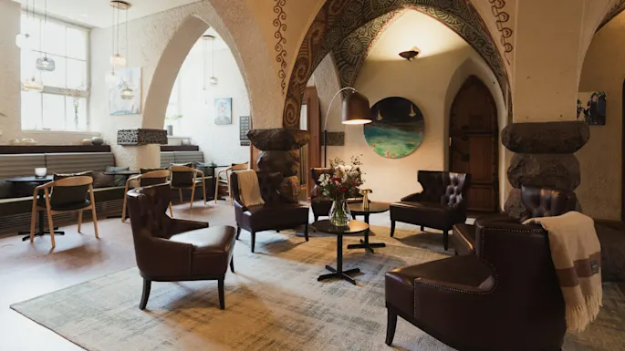 Elegante skinnstoler arrangert rundt et bord med friske blomster, i et koselig rom med buede tak, dekorative elementer og veggkunst. Myk belysning skaper en varm atmosfære.