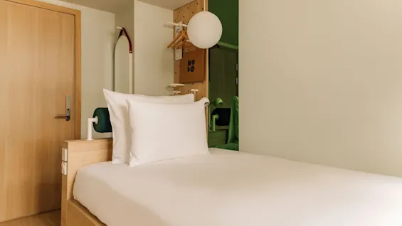 A modern, minimalist hotel room with a single bed, light wood accents, and a sign that reads HOBO.