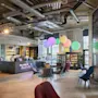 Reception desk staffed by two people, surrounded by colorful chairs and large hanging balloons in a modern lounge area. Text on the desk reads: "Keys, drinks and Rock’n’Ro."