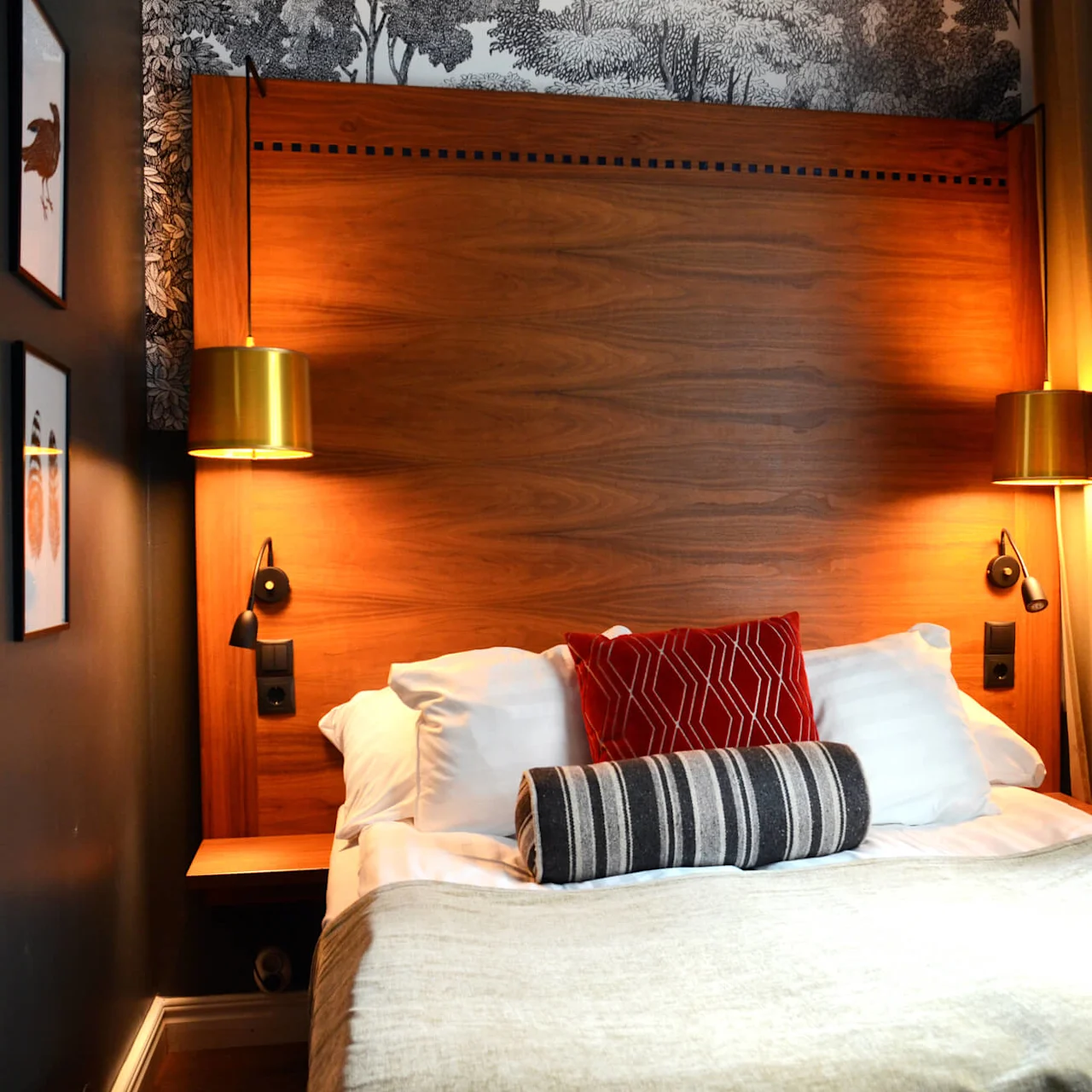 A neatly made bed with pillows and a wooden headboard, flanked by golden lamps, in a cozy room.