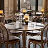 Runt träbord dukat med glas, servetter och blommor i en svagt upplyst restaurang med böjda stolar och stämningsbelysning.