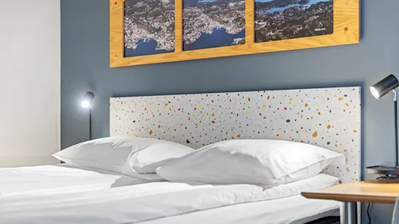 An unmade bed with white bedding in a room with terrazzo-style headboard and framed pictures above.