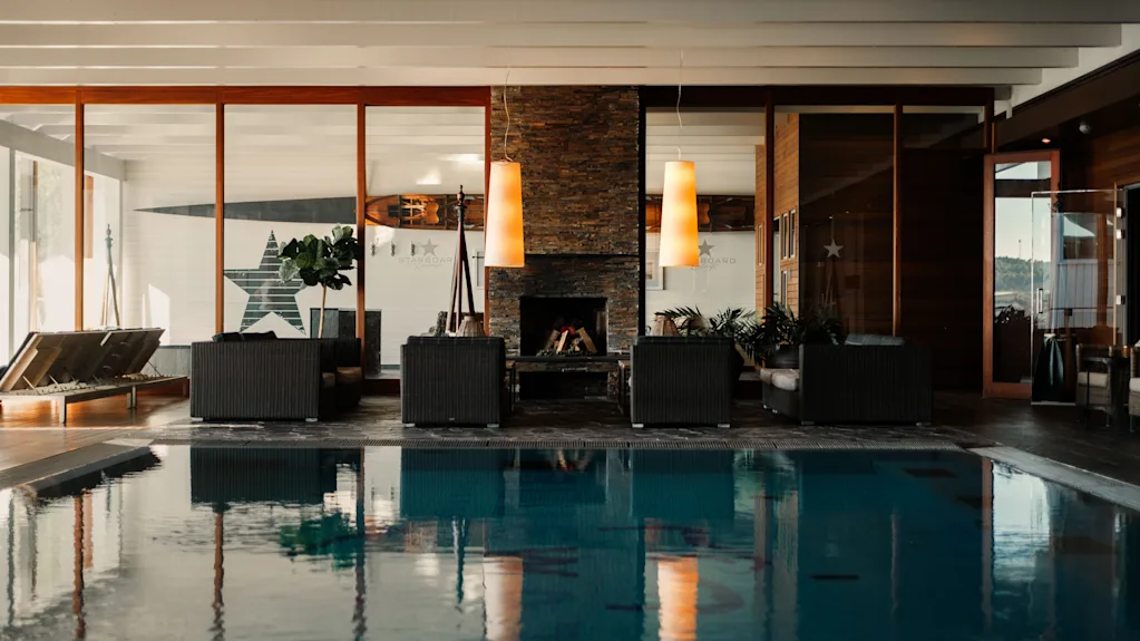 Et luksuriøst indendørs poolområde med en hyggelig lounge, pejs og store vinduer, der tilbyder en afslappende atmosfære.