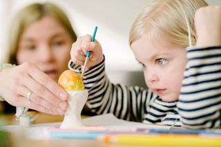 Girl painting easter eggs with mother