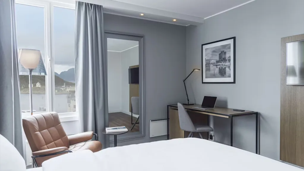 Lyst og moderne hotellrom med skrivebordsplass, lenestol ved vinduet og en behagelig seng.