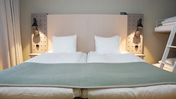 Mukava hotellihuone, jossa kaksi sänkyä, puinen sängynpääty integroidulla valaistuksella ja vilahdus kerrossängystä.