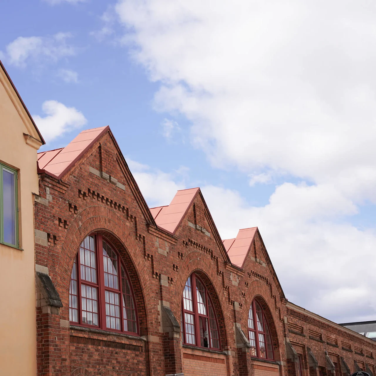 Historiska tegelbyggnader med bågformade fönster och kontrasterande gul fasad under en molnig himmel.