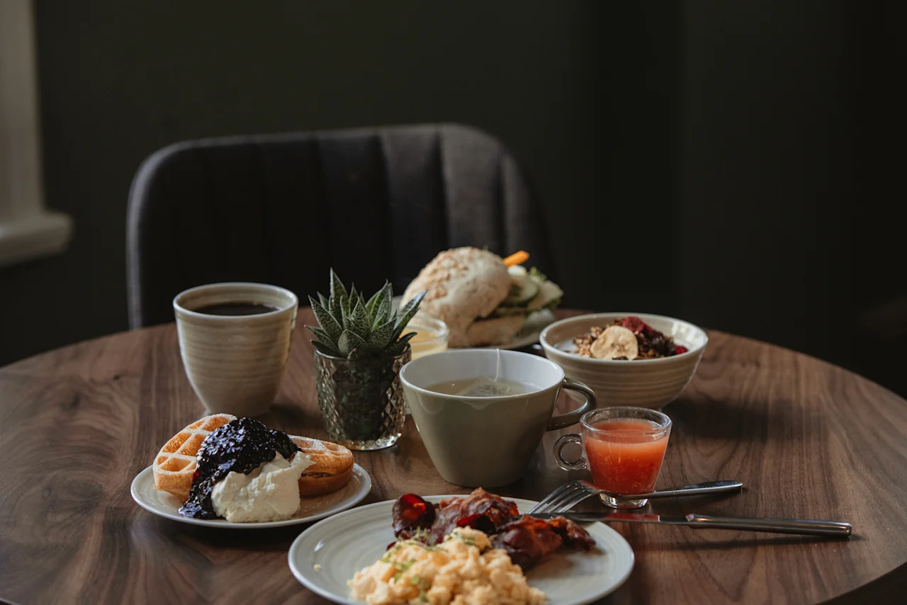 A delightful breakfast spread on a wooden table, featuring waffles, scrambled eggs, bacon, and various drinks. Home Hotel Post.