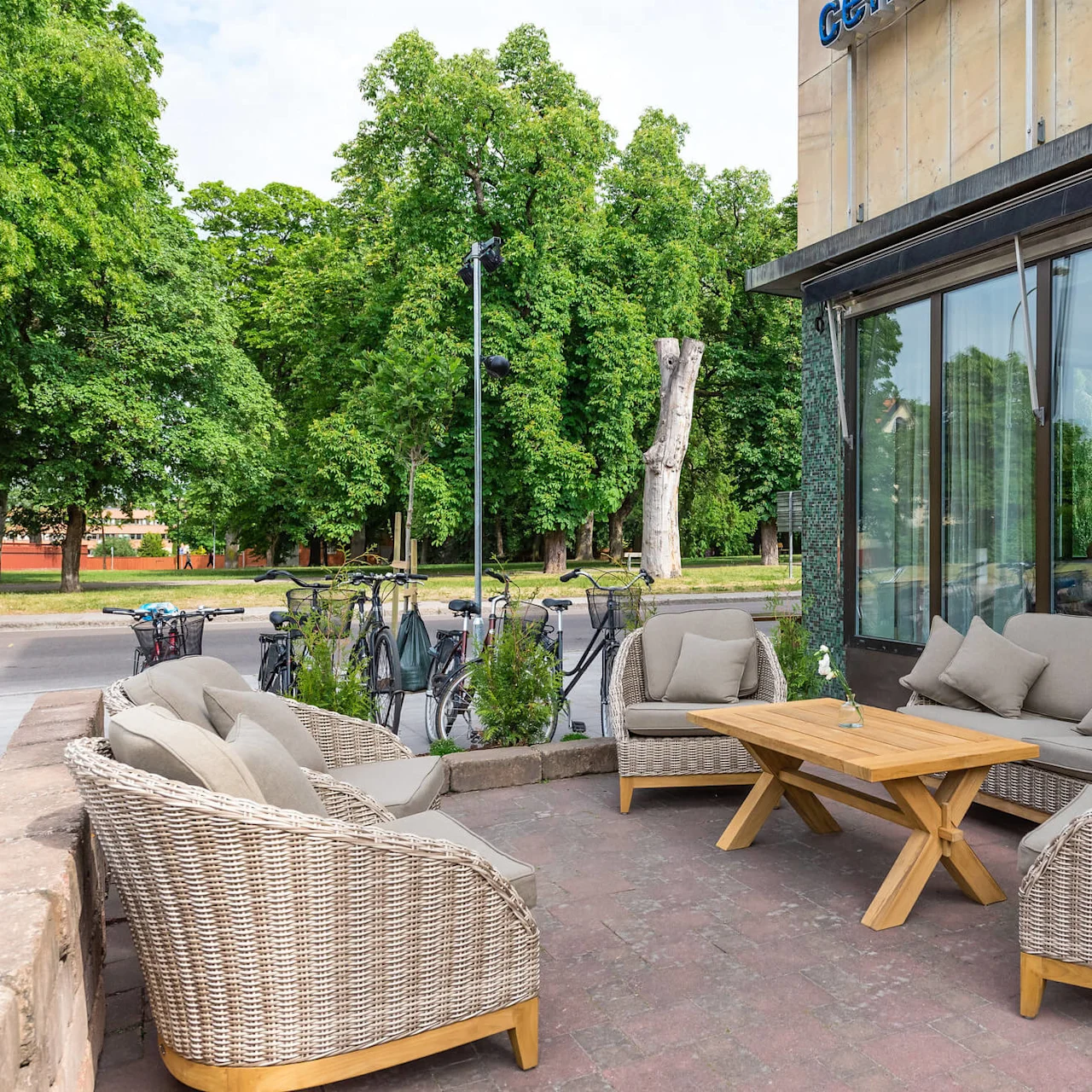 Utemöbler står framför ett modernt café, med träd och en cykelställning i bakgrunden.
