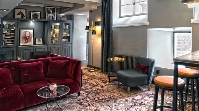 En stilig salong med en luksuriøs rød sofa, kuraterte bokhyller, innrammede portretter og stemningsfull belysning gir en koselig atmosfære.