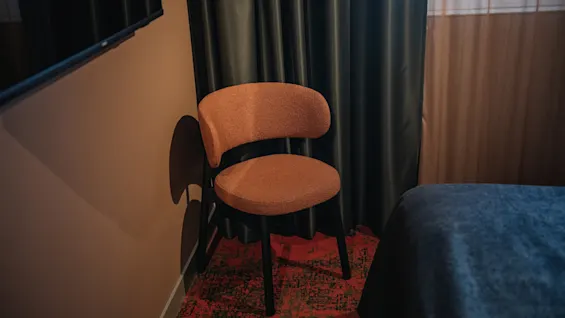 Et komfortabelt hotellrom med en stilig stol, en pent oppredd seng og mørke gardiner, som antyder et avslappende opphold.