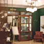 En ljuskrona hänger i en hotellobby med marmorgolv, bruna stolar och orkidéer i krukor. En skylt lyder "DROTT BAR" ovanför en dörr av glas.