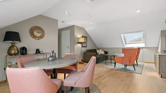 Home Hotel Gabelshus. Et lyst og innbydende oppholdsrom med spisebord, komfortable sitteplasser og et takvindu.