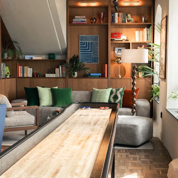 A comfortable and stylish lounge area with a shuffleboard table, a sofa with colorful cushions, and built-in bookshelves.