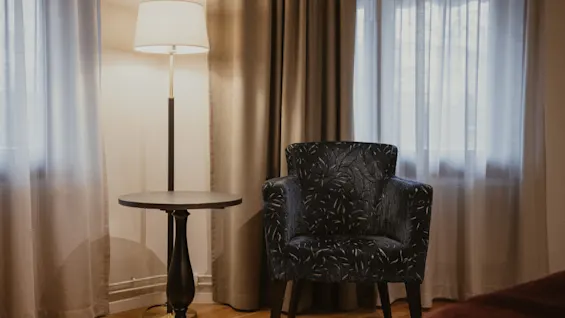 A cozy reading nook with an armchair, a side table, and a floor lamp, at Home Hotel Kung Oscar.