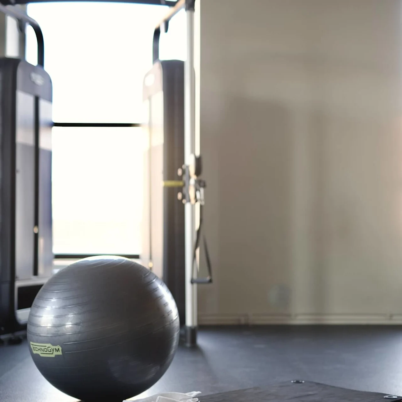 A fitness ball, dumbbells, and a workout mat on a gym floor, suggesting an exercise setting with equipment ready for use.