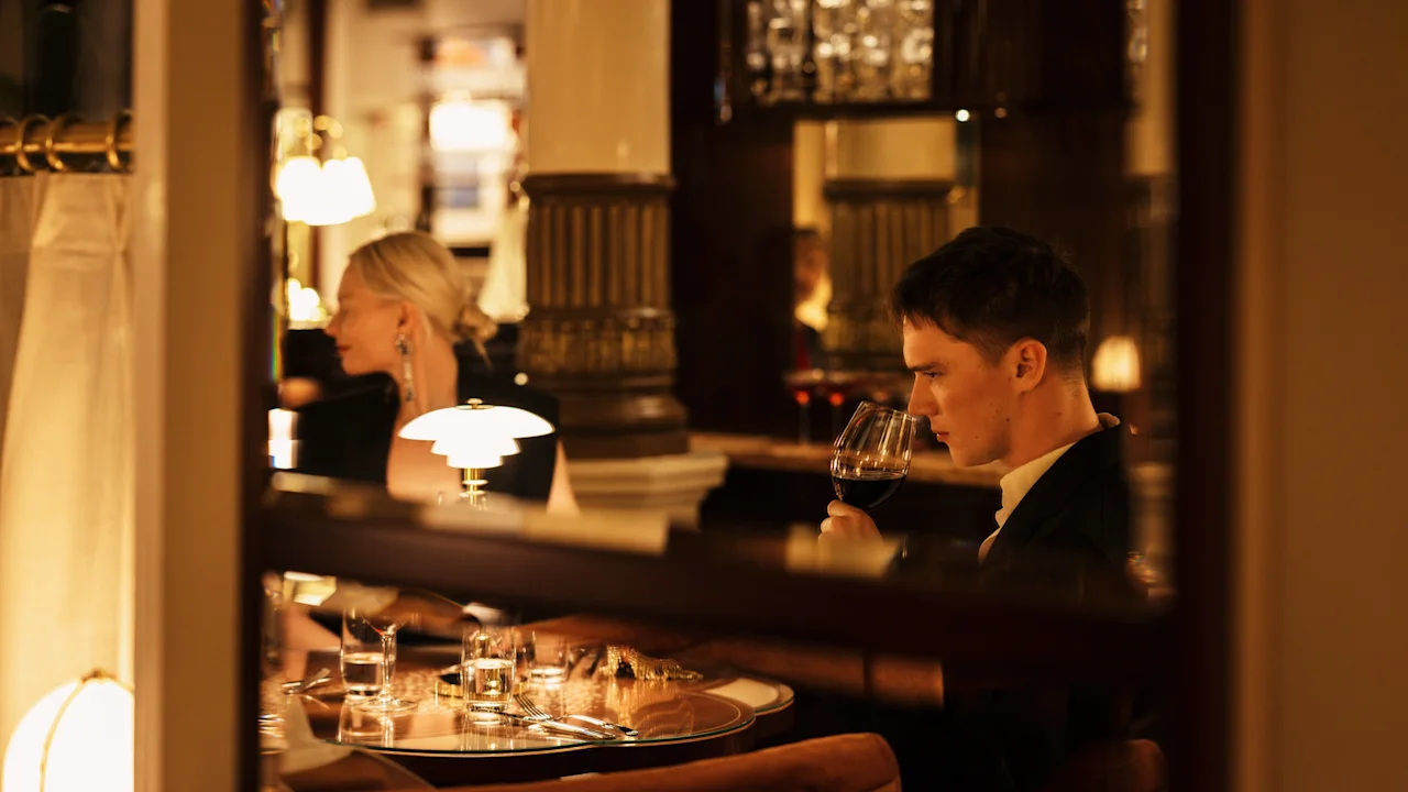 An individual enjoying a glass of red wine in a sophisticated bar environment. Hotel Kämp – Kämp Bar.