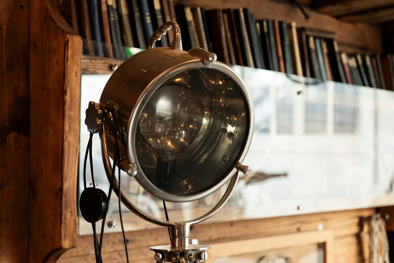 En vintage spotlightlampe med et varmt skær, placeret mod en sløret baggrund af bøger på en træhylde.