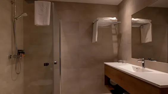 Ett modernt hotellbadrum med en dusch, ett handfat med spegel och rena handdukar.