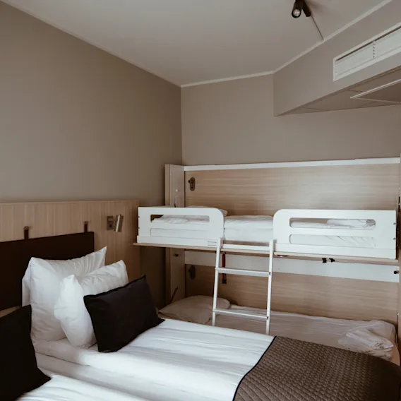 Ett modernt och bekvämt hotellrum med en stor säng och en inbyggd våningssäng, designat för flera gäster.