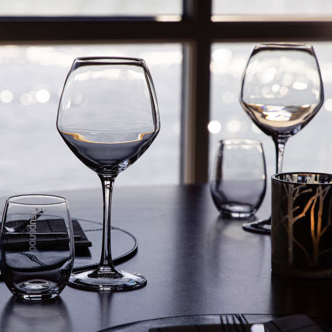 Empty wine glasses on a table, silhouetted against a bright window, implying a dining setting.