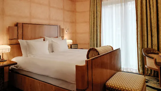 En pent oppredd seng i et godt opplyst rom med elegant dekor og draperte vinduer.