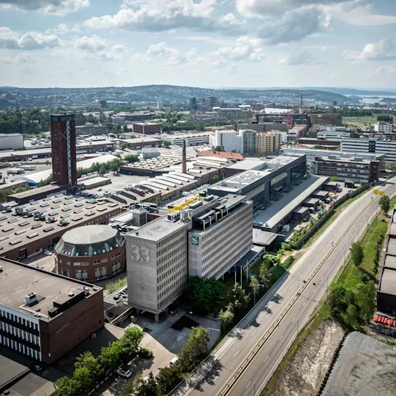 Bygning med "33" på står midt i et vidstrakt industriområde, omgitt av veier og andre store bygninger, under en delvis skyet himmel.