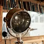 En vintage spotlightlampe med et varmt skær, placeret mod en sløret baggrund af bøger på en træhylde.