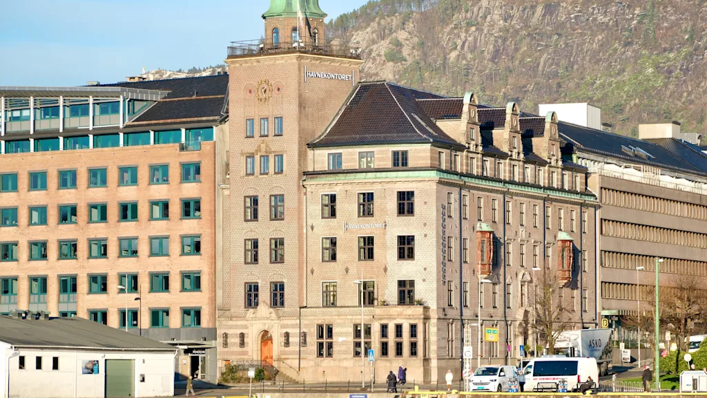 A charming waterfront scene featuring a historic building with a green dome and the text HAVNEKONTORET, against a mountain backdrop.